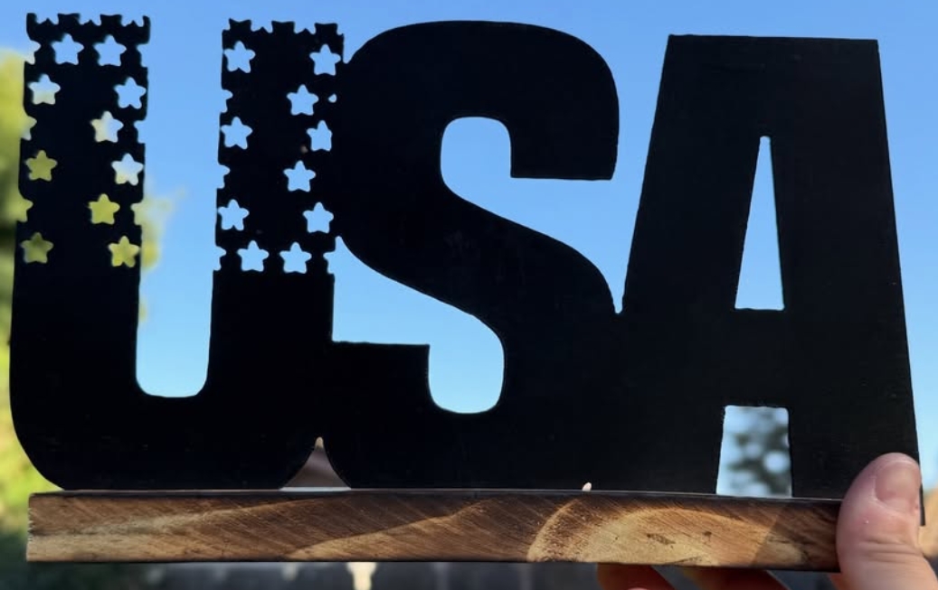 A steel USA sign with a star-cut flag, mounted on a wood base.