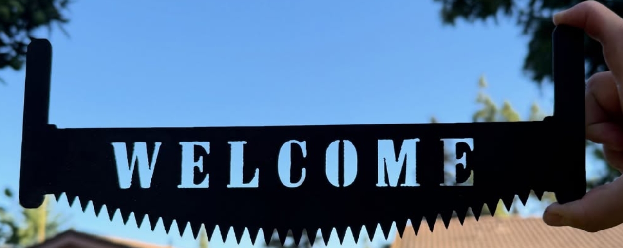 A steel WELCOME sign cut from a saw blade, held against a blue sky.