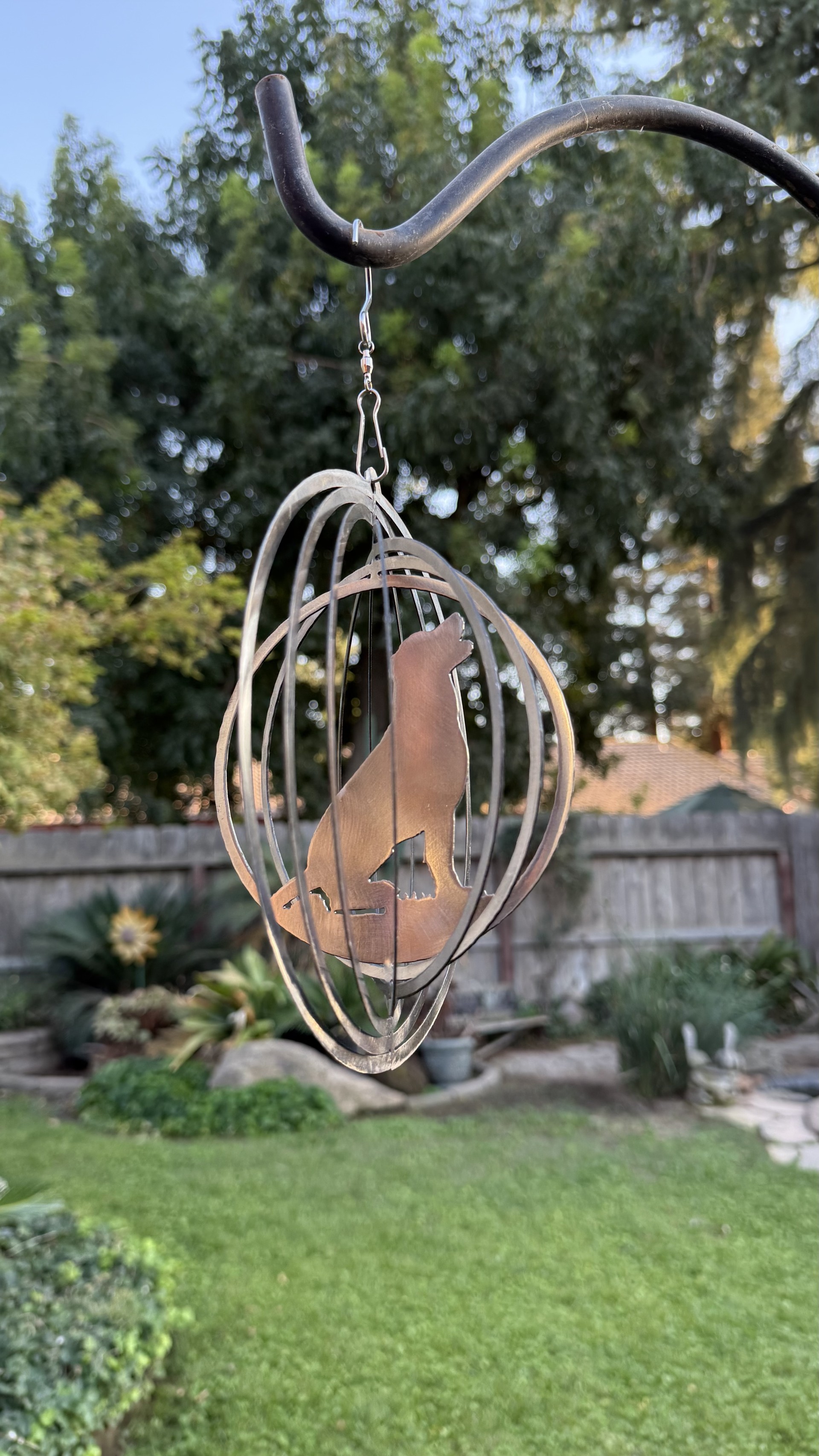 A copper wolf wind spinner turning on a hook in a backyard.