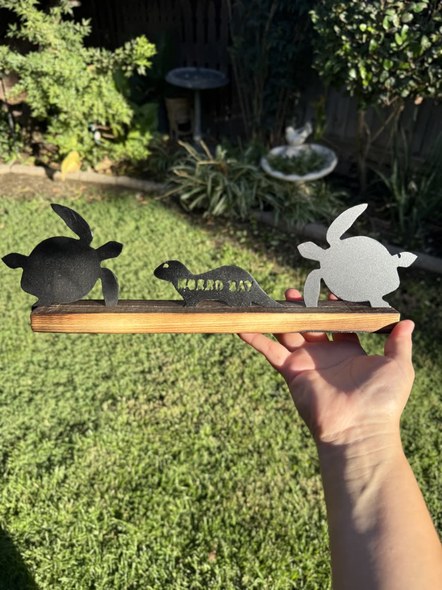 Two turtles and an otter cut from steel on a wooden base.