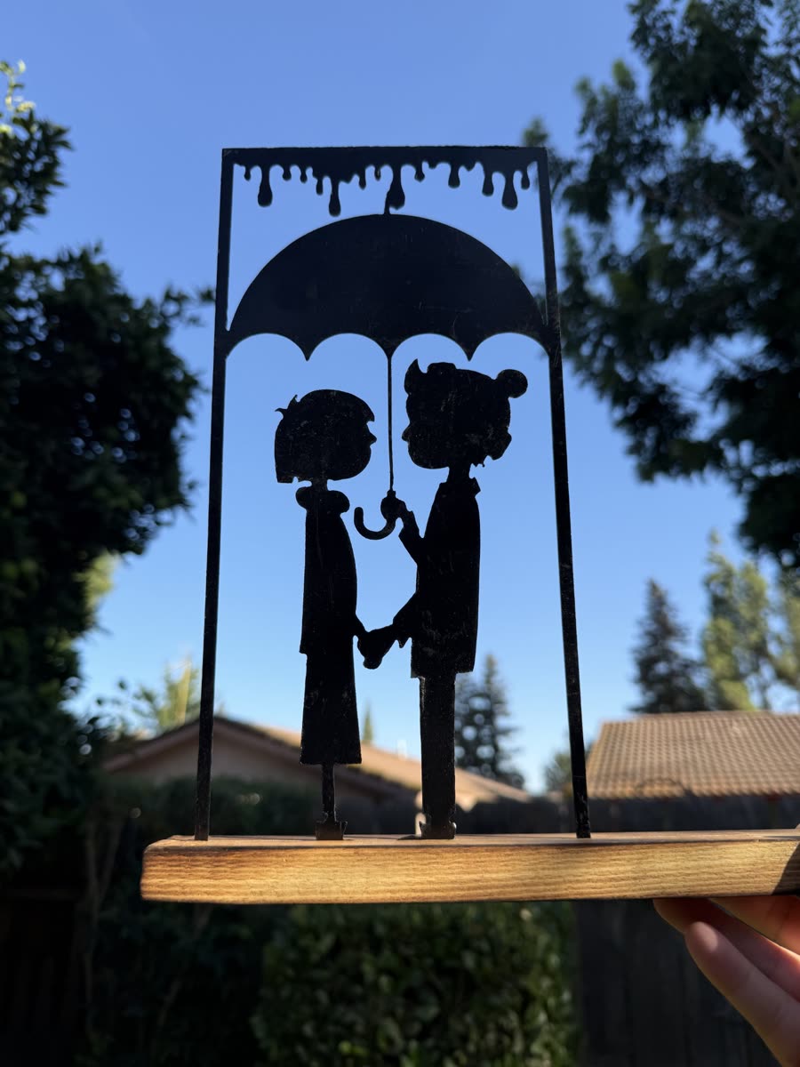 Two figures holding hands under an umbrella in the rain, cut from steel.